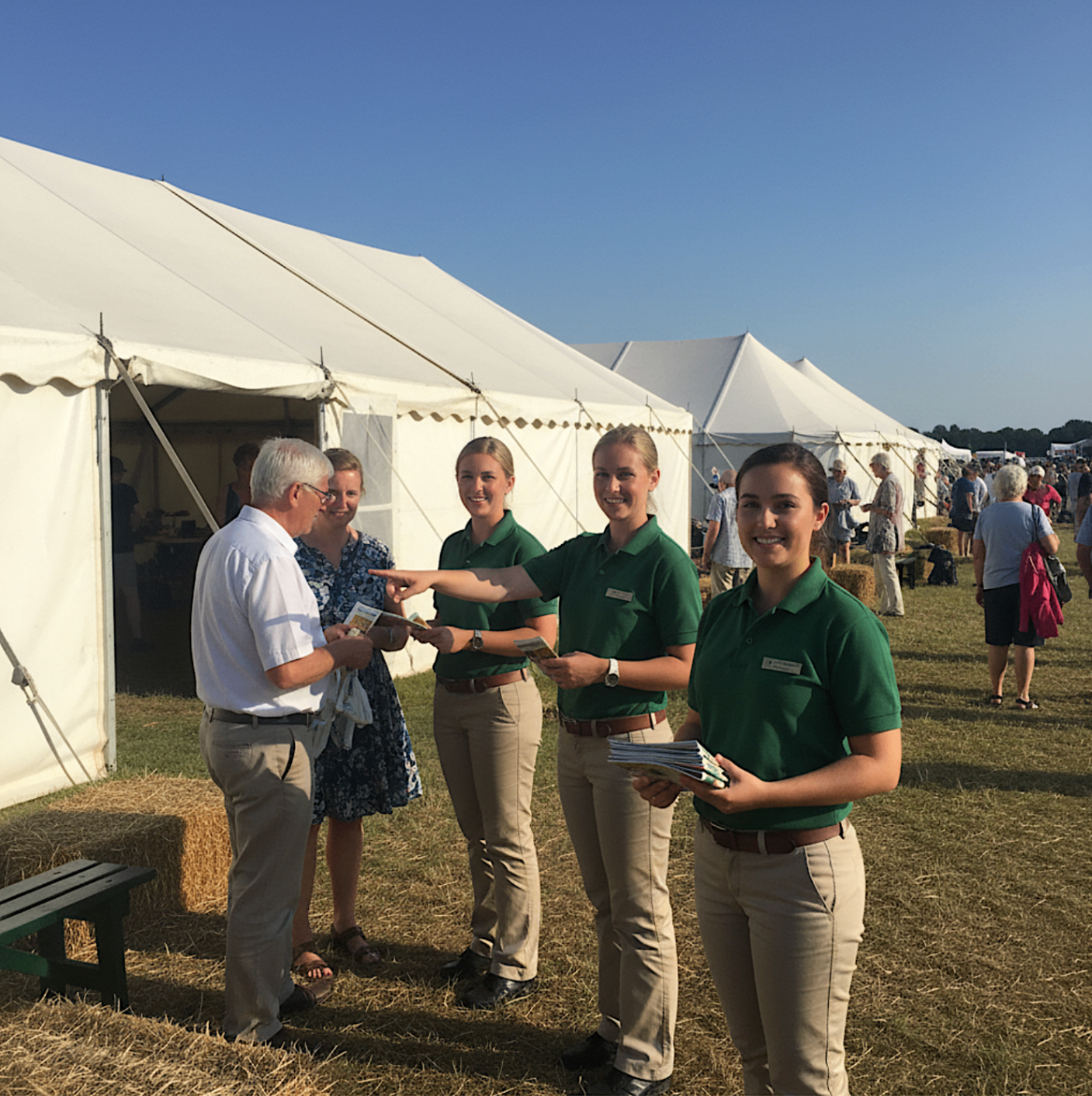 Event hosts welcoming guests and handing out programmes beside festival tents